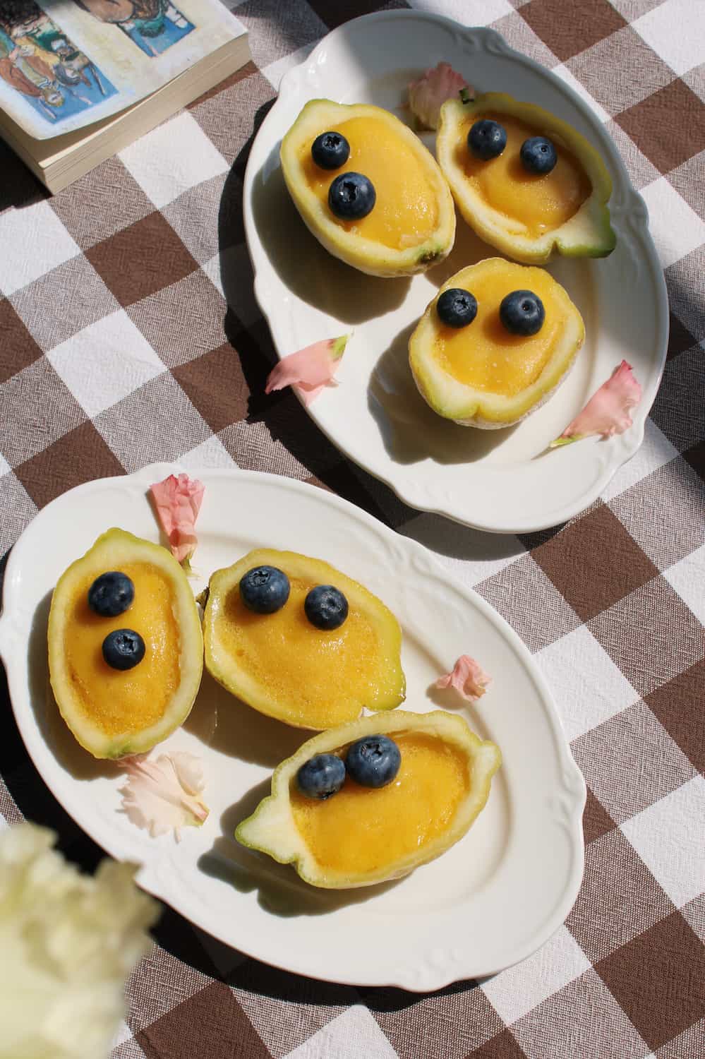 Auriel oval serving plate in white ceramic with scalloped rim, styled with mango halves and blueberries on a checkered linen