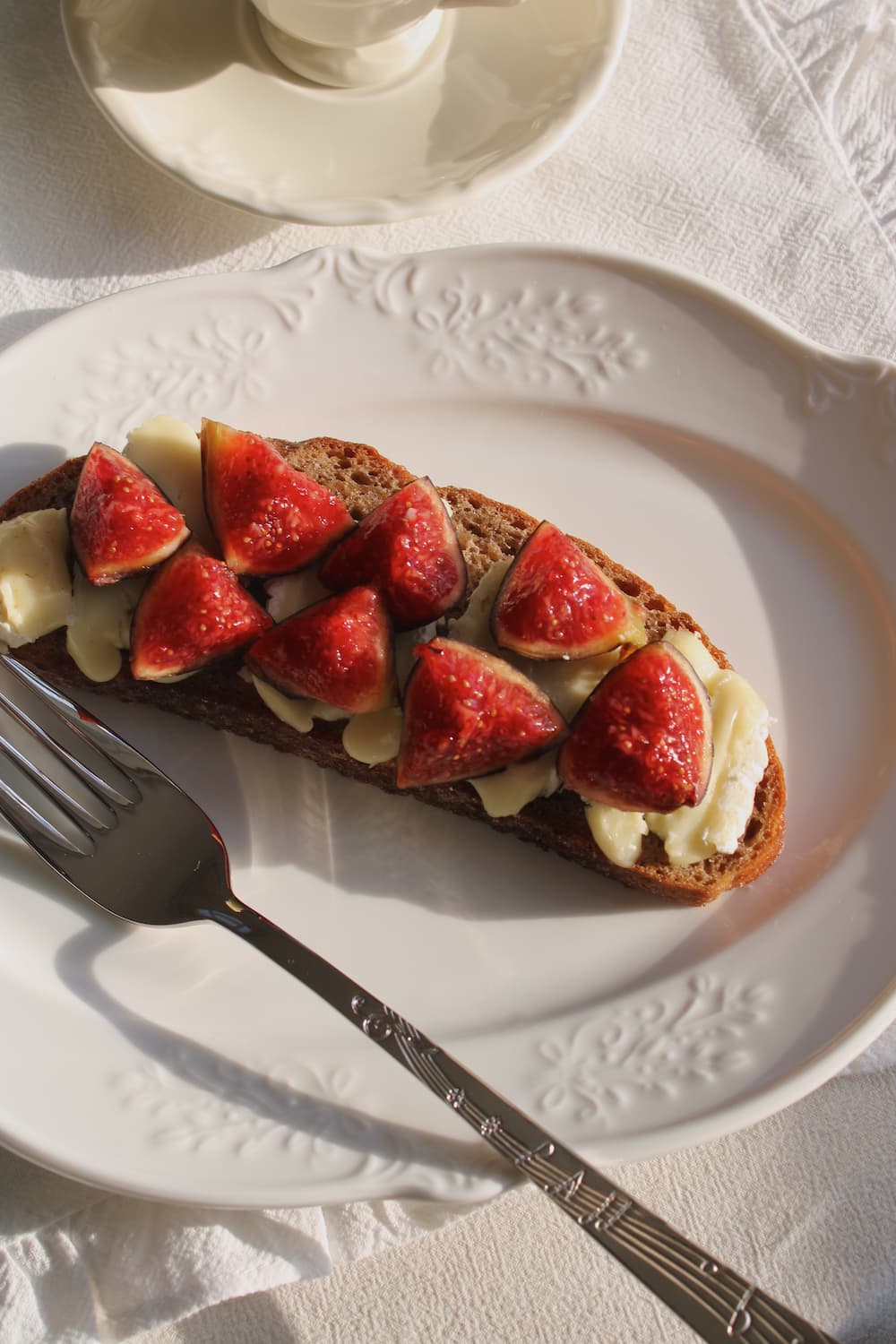 Toast with sliced strawberries and cream cheese on a white plate with a fork.