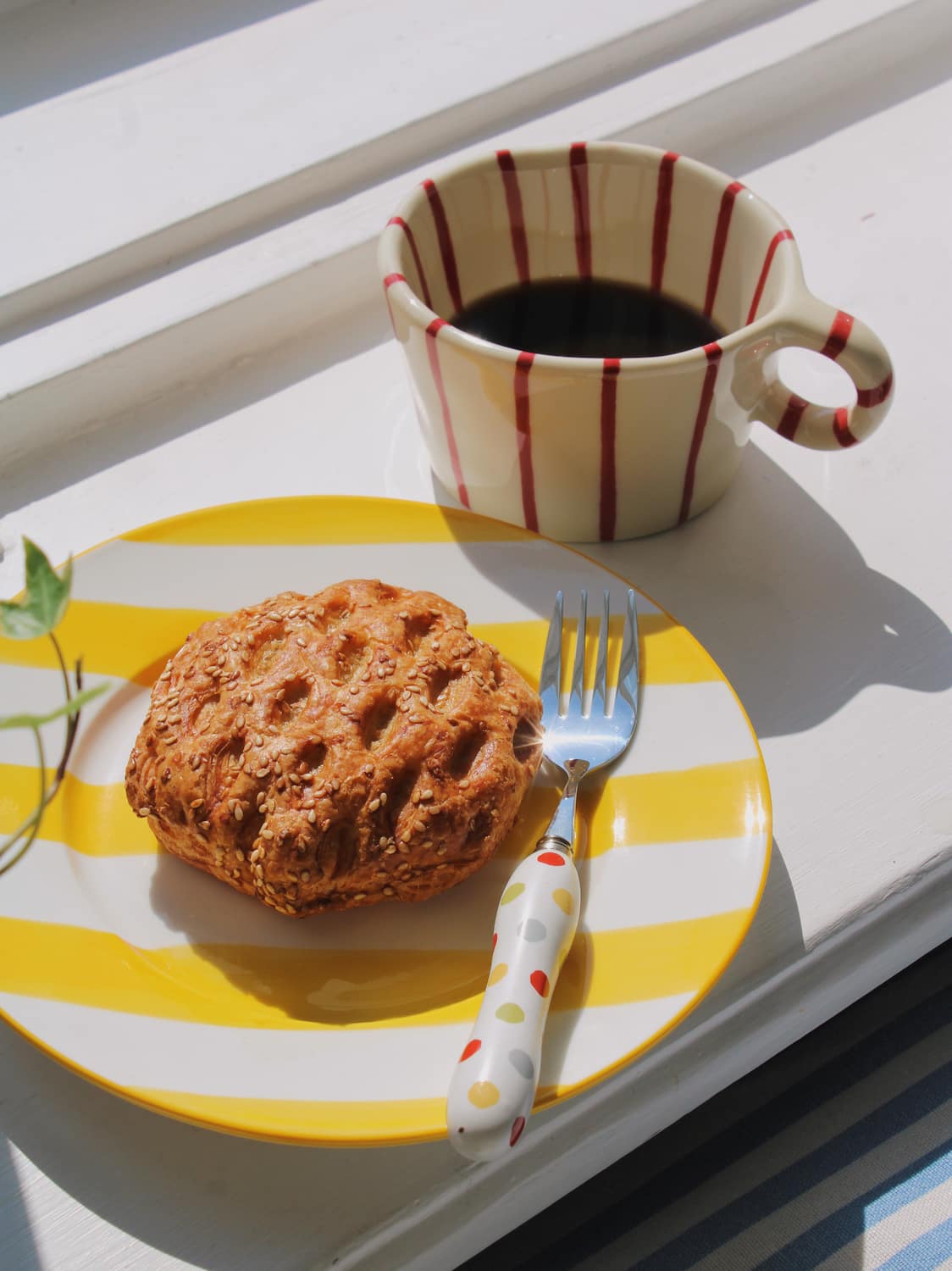 Etta Ceramic Plate in yellow with bold stripe pattern and Arlo mug styled with a sesame pastry and the Confetti Cutlery Set fork 