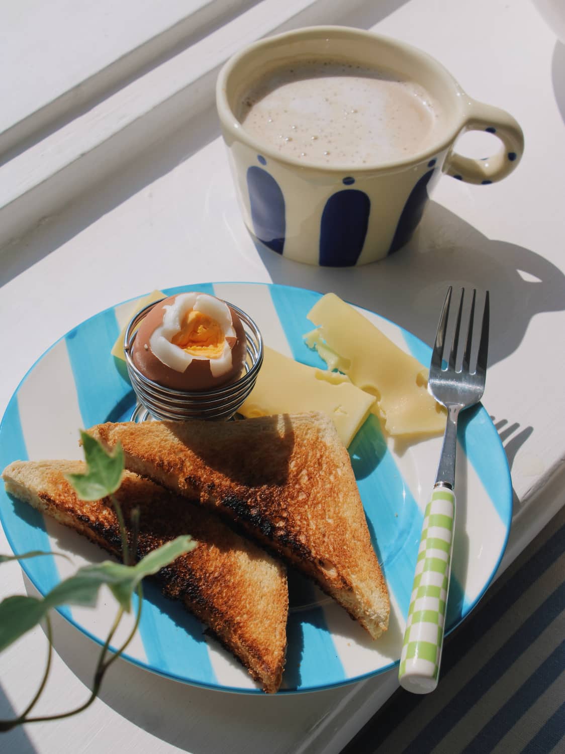 Mirel Ceramic Plate in white with bold blue stripe pattern, styled with toast, a soft boiled egg and cheese slices on a blue striped surface.