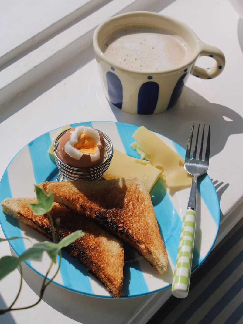 Mirel Ceramic Plate in white with bold blue stripe pattern, styled with toast, a soft boiled egg and cheese slices on a blue striped surface.