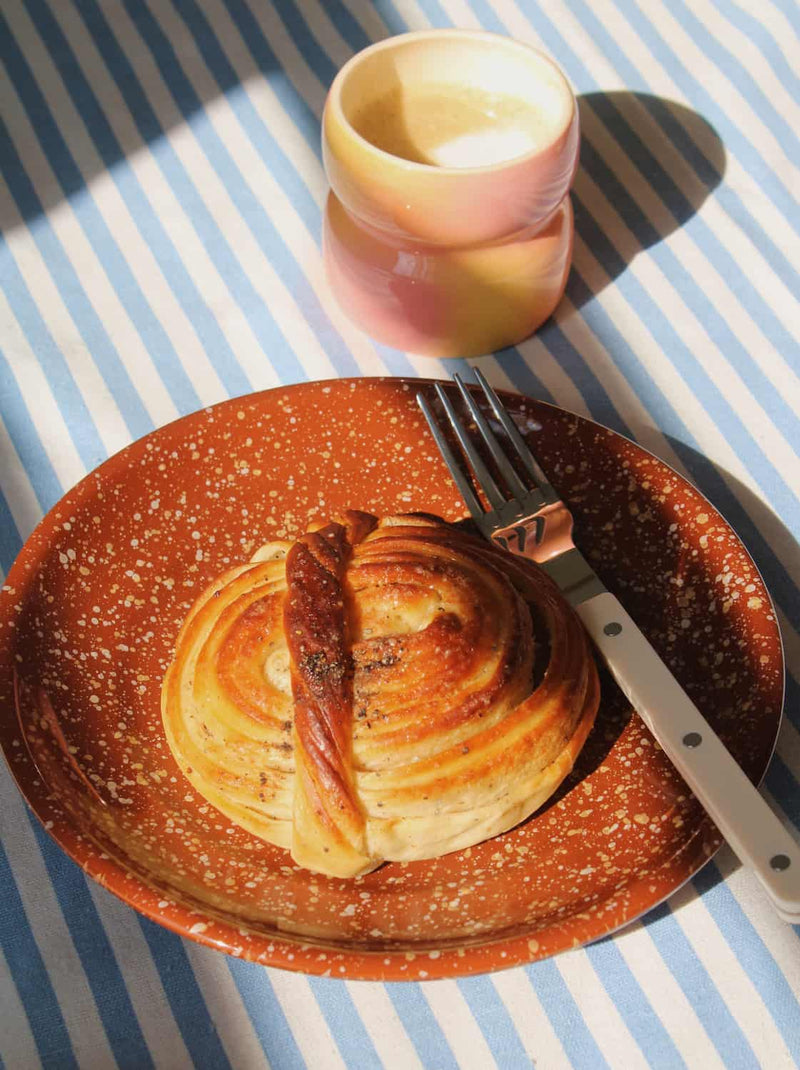 Speckled ceramic plate with croissant and coffee cup, warm-toned handmade tableware for breakfast setting