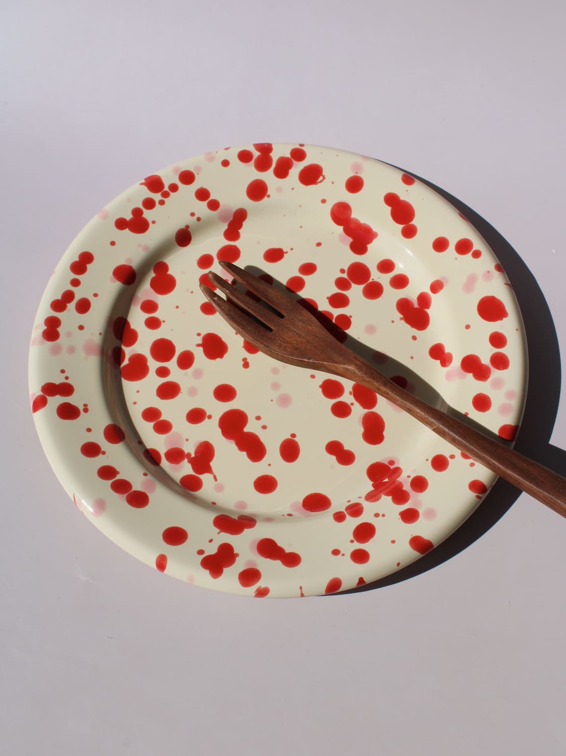 Dotty Ceramic Plate in cream with red speckled dot pattern, viewed from above on a soft pink background.