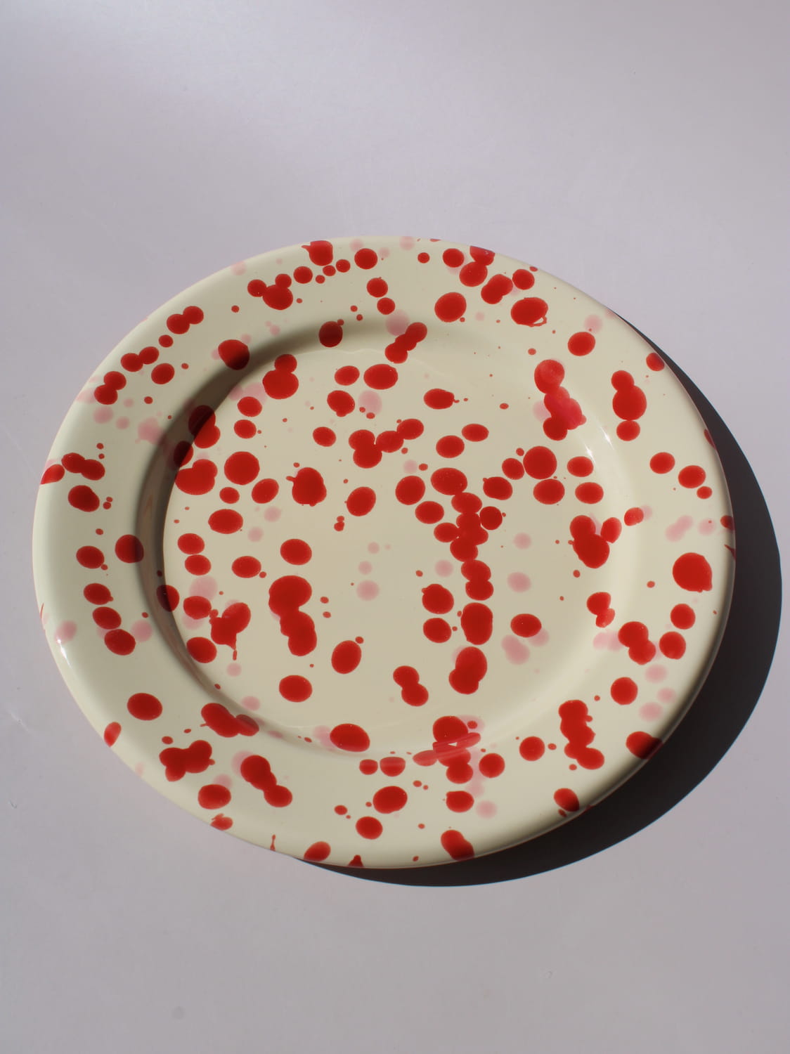 Dotty Ceramic Plate in cream with red speckled dot pattern, viewed from above on a soft pink background.