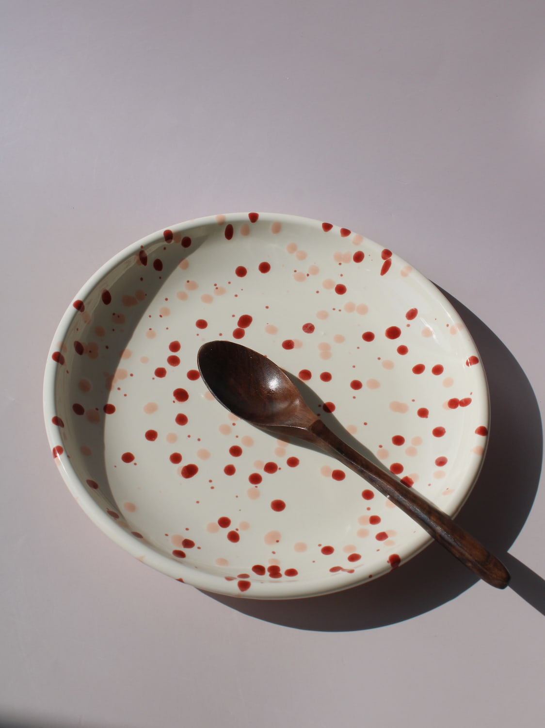 Bera Ceramic Plate in cream with red speckled dot pattern, paired with a wooden fork, viewed from above on a soft pink background.