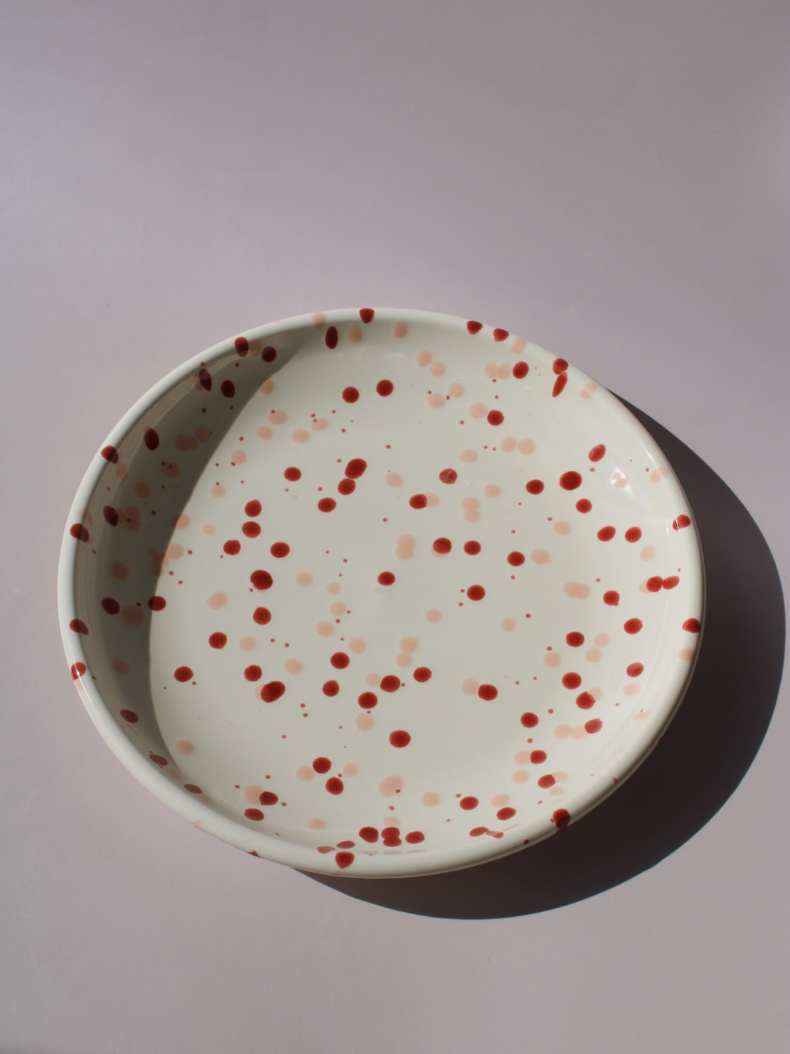 Bera Ceramic Plate in cream with red speckled dot pattern, paired with a wooden fork, viewed from above on a soft pink background.