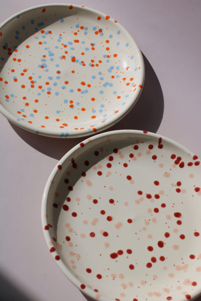 Bera and Naro Ceramic Plate in cream with red speckled dot pattern, paired with a wooden fork, viewed from above on a soft pink background.