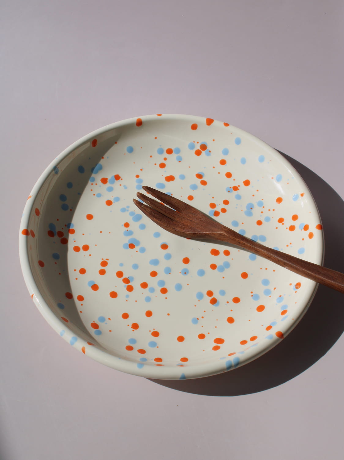Naro Ceramic Plate in cream with orange and blue speckled dot pattern, viewed from above on a soft pink background.