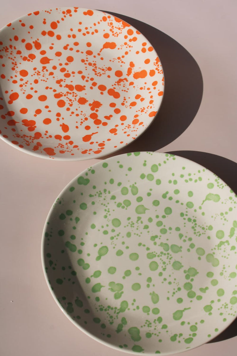 Hand-speckled ceramic plates in orange and green splatter glaze, modern enamel-style tableware.