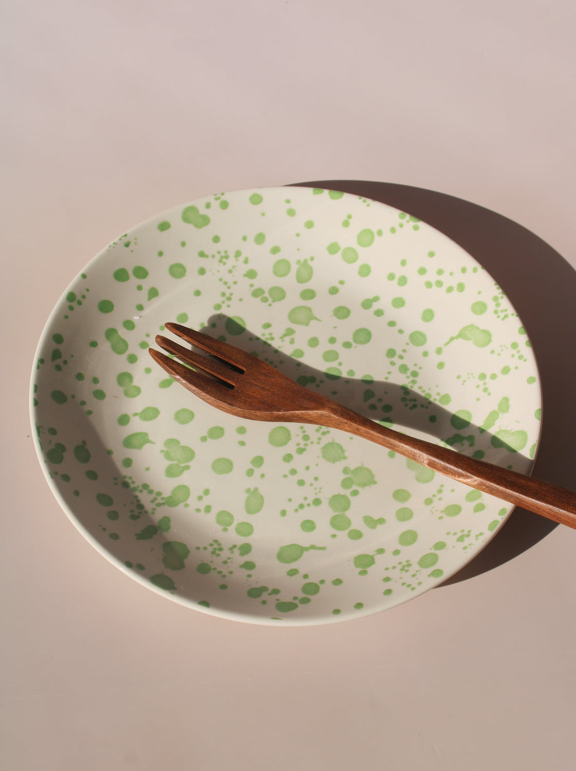 Green splatter ceramic dinner plate with painterly speckled glaze finish.