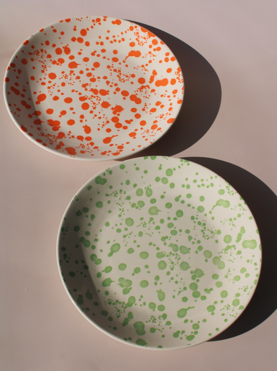 Hand-speckled ceramic plates in orange and green splatter glaze, modern enamel-style tableware.