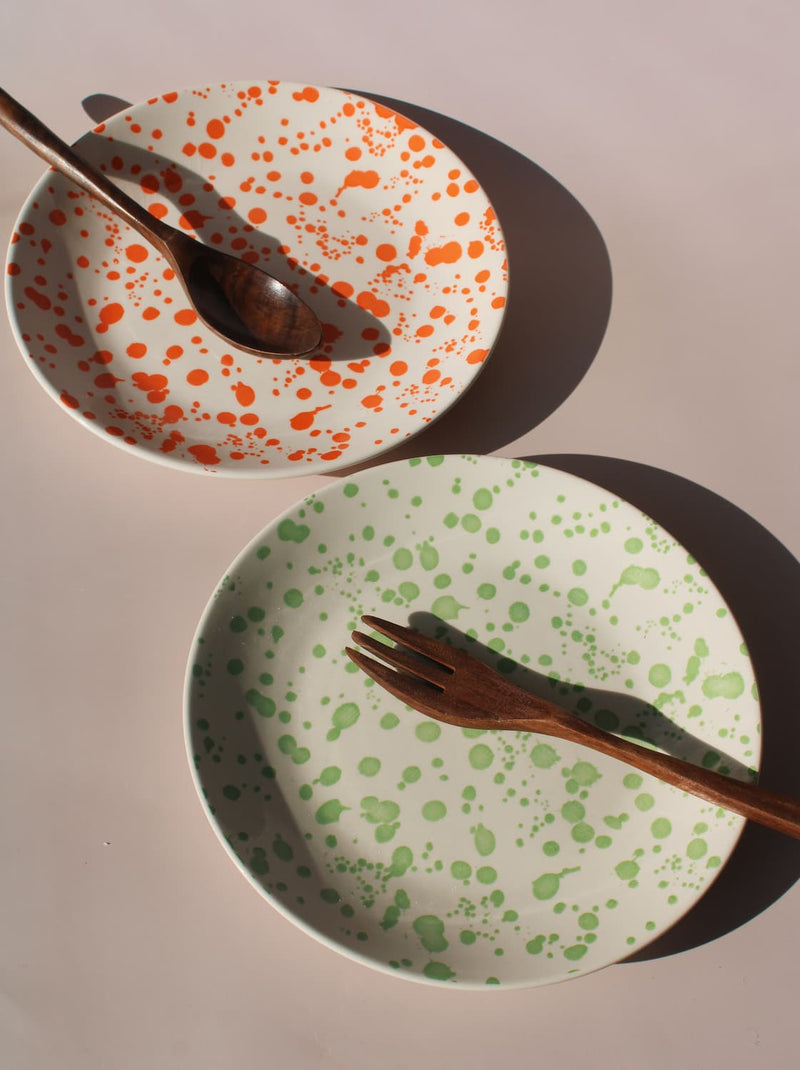 Hand-speckled ceramic plates in orange and green splatter glaze, modern enamel-style tableware.