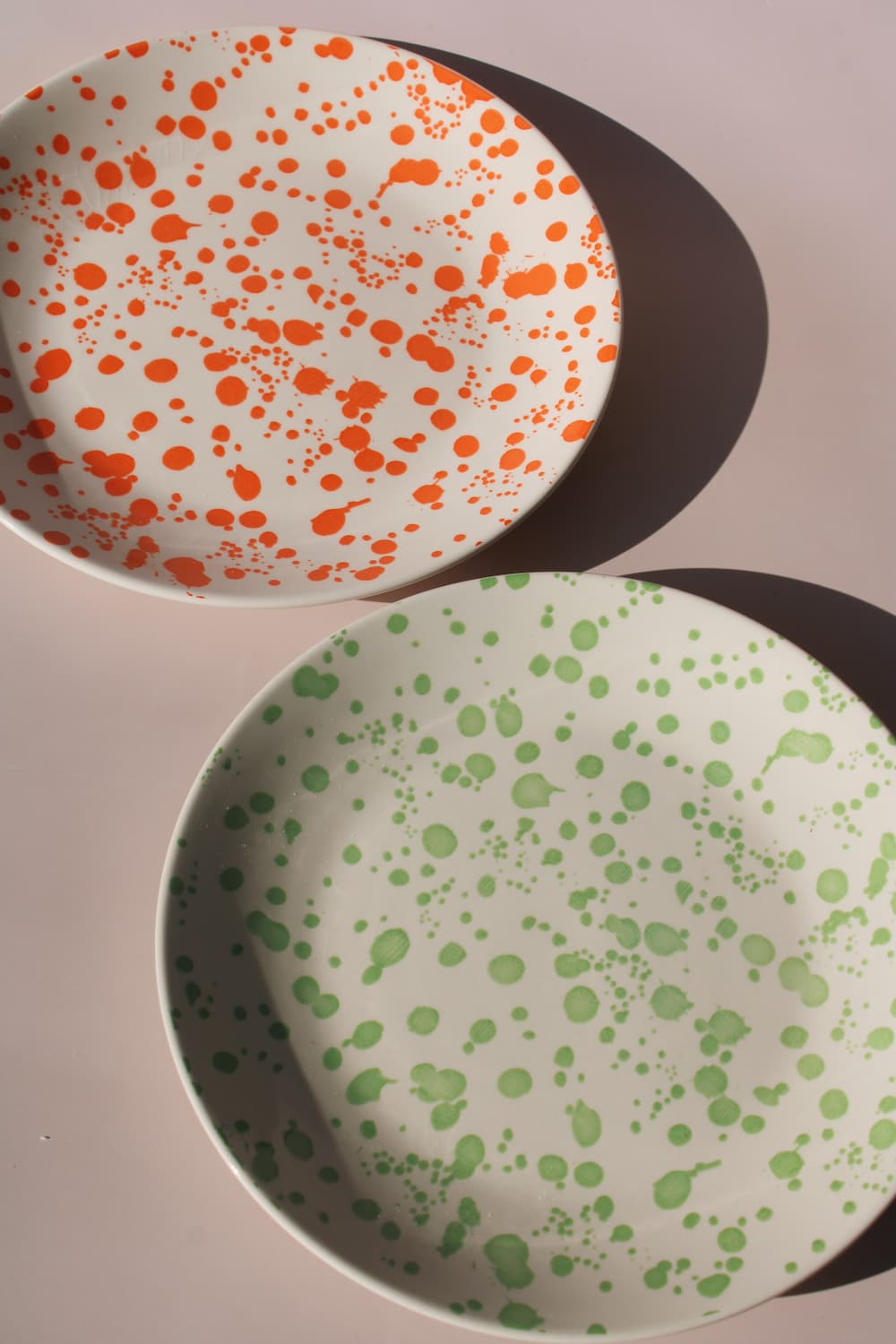 Hand-speckled ceramic plates in orange and green splatter glaze, modern enamel-style tableware.