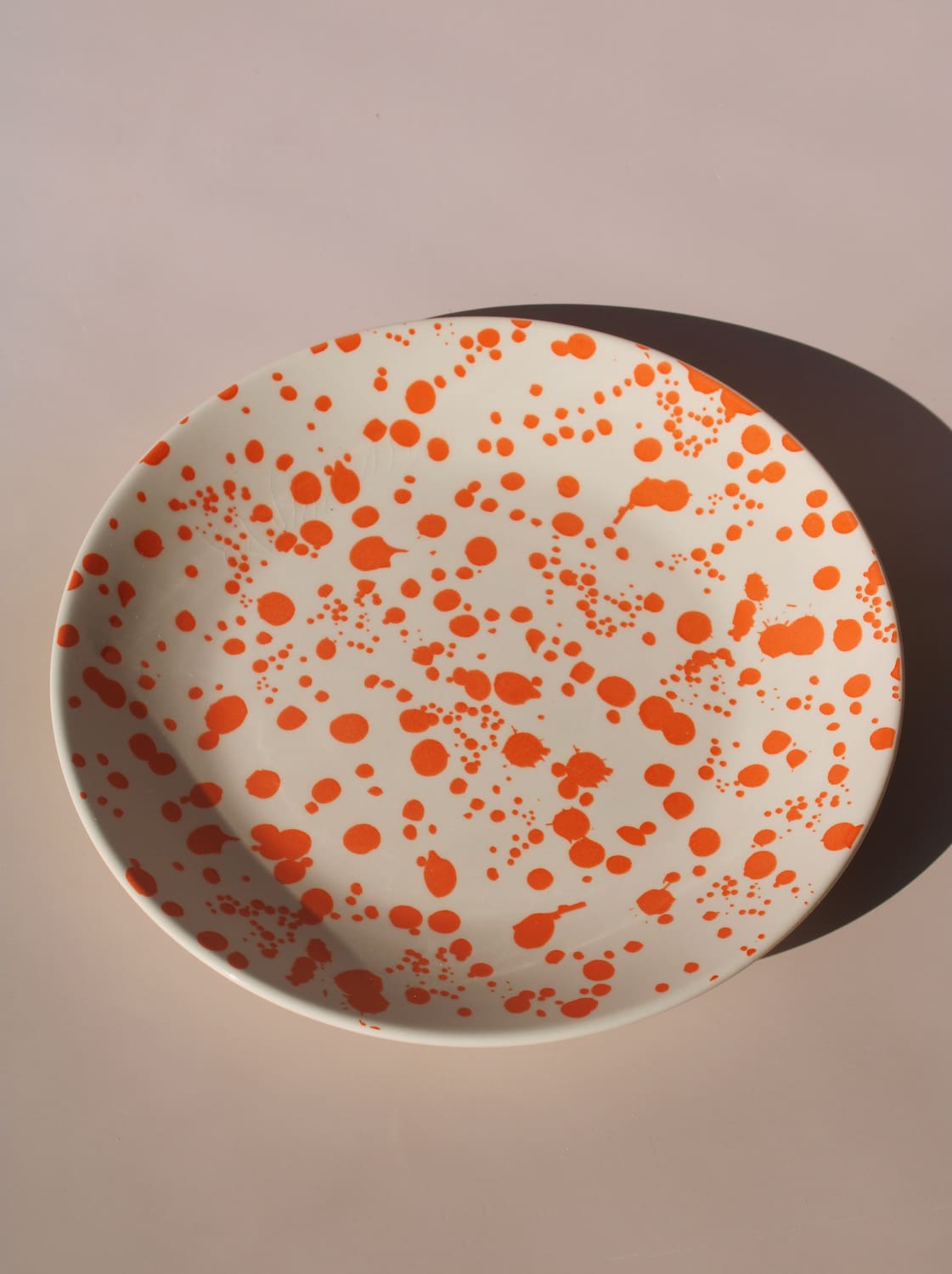 Orange splatter ceramic dinner plate with hand-applied speckled glaze pattern.