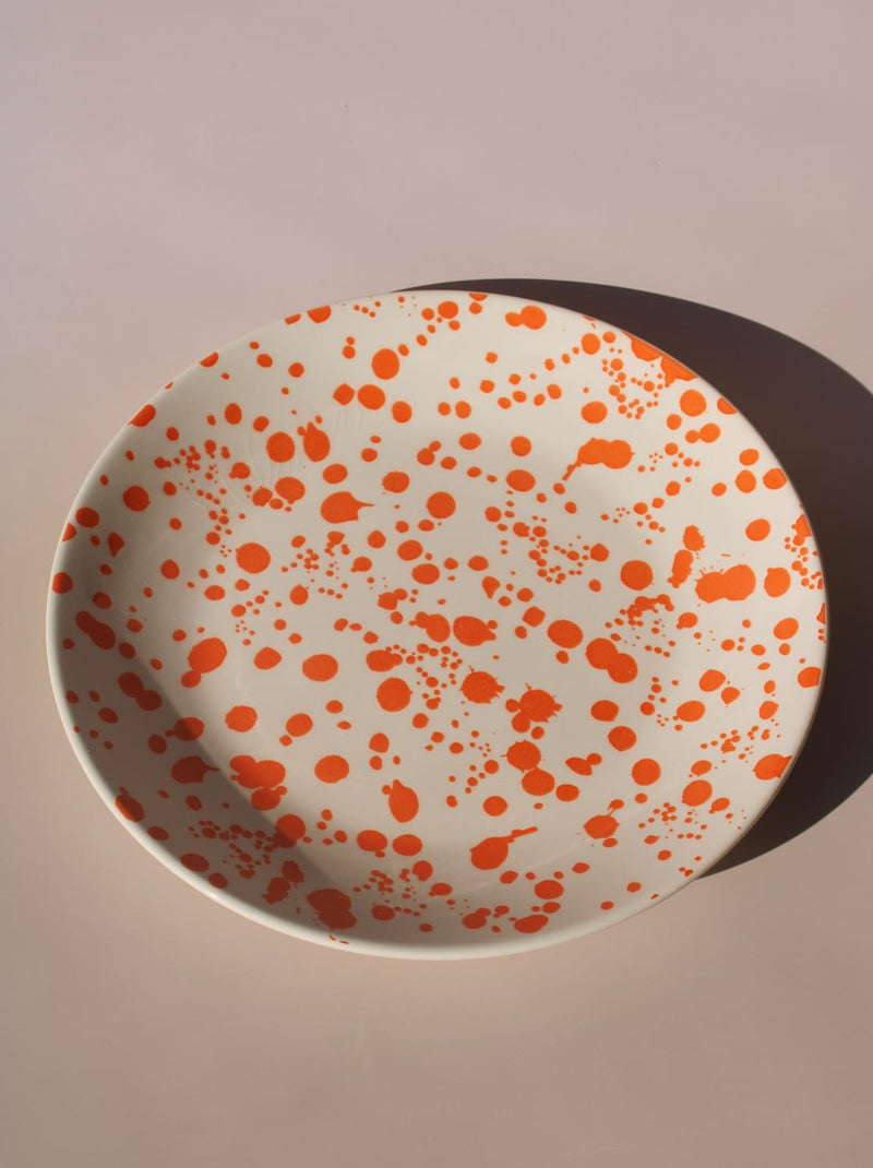 Orange splatter ceramic dinner plate with hand-applied speckled glaze pattern.
