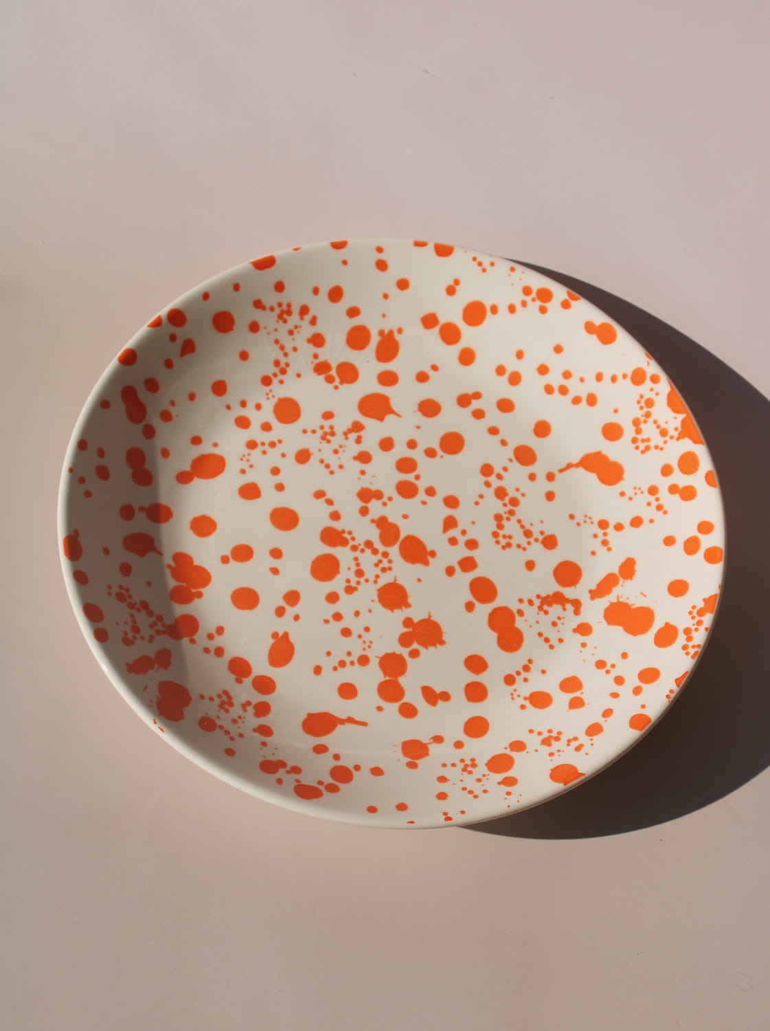 Orange splatter ceramic dinner plate with hand-applied speckled glaze pattern.