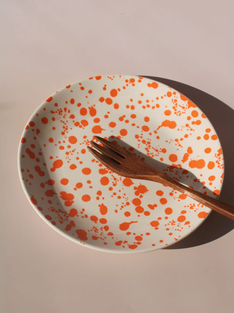 Orange splatter ceramic dinner plate with hand-applied speckled glaze pattern.