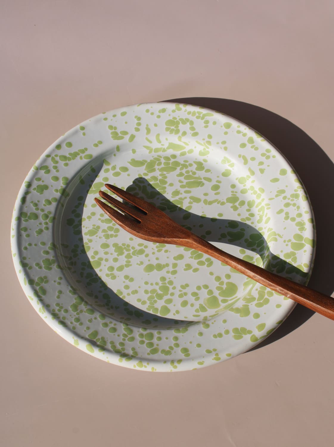 Green splatter enamel plate with retro speckled pattern in soft natural lighting.