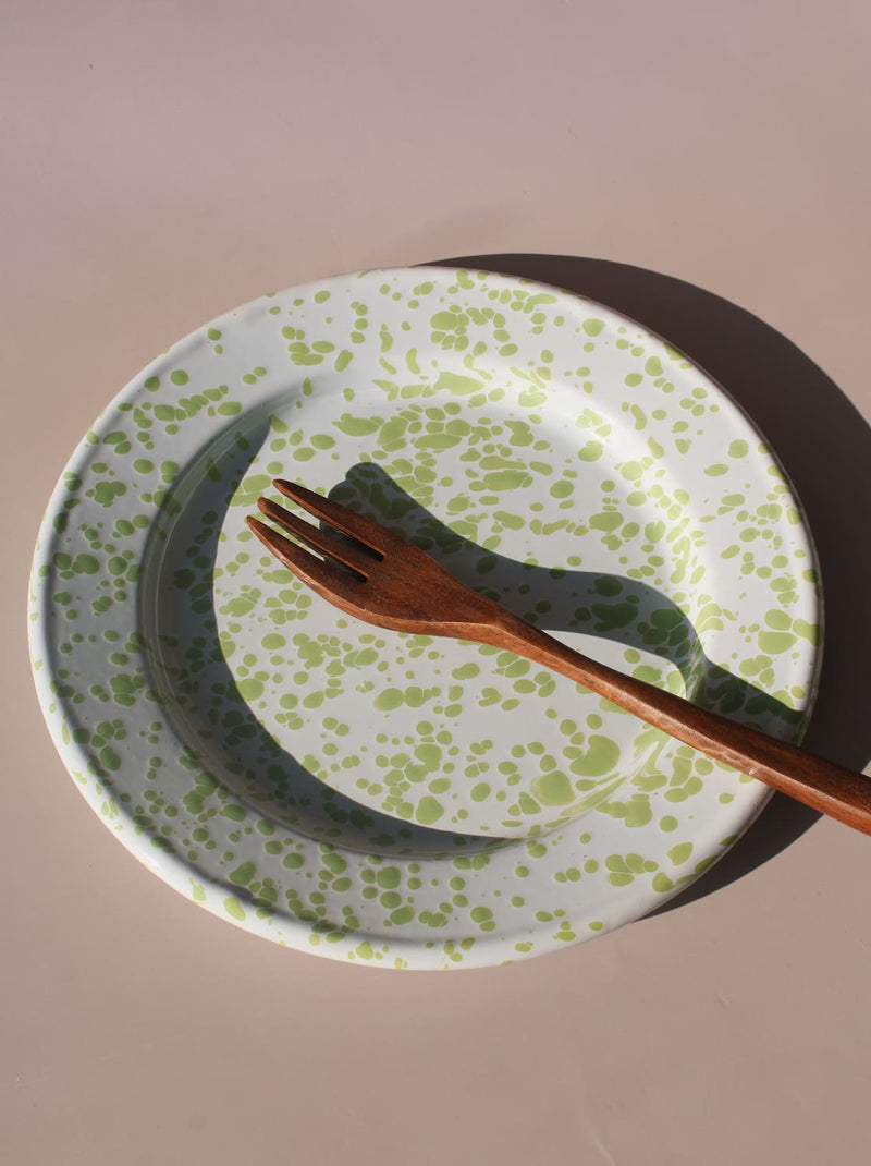 Green splatter enamel plate with retro speckled pattern in soft natural lighting.