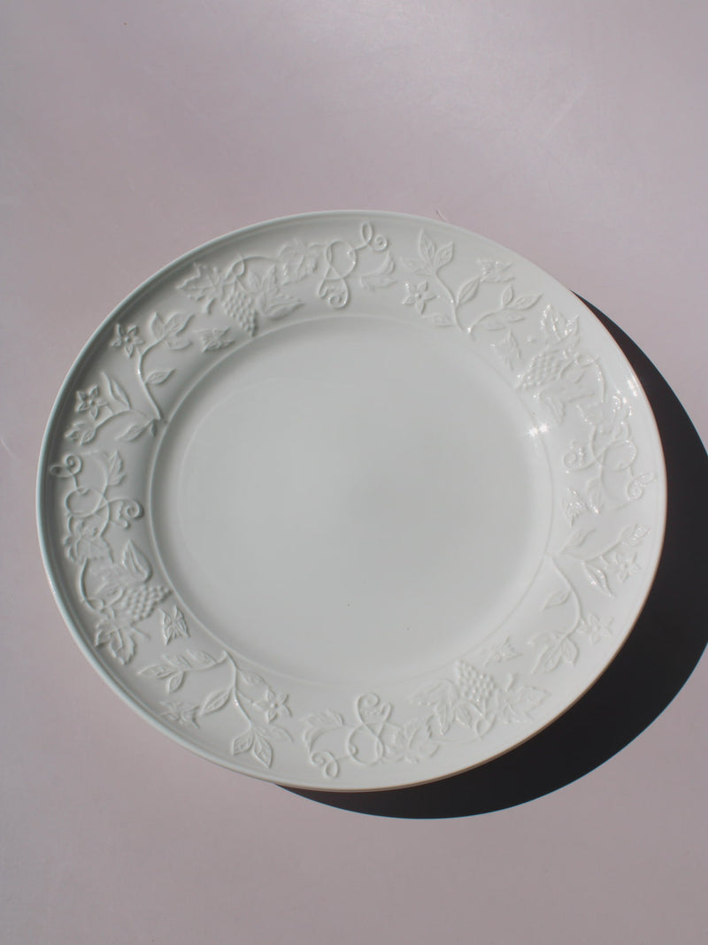 Florentia Ceramic Plate in white with embossed floral and botanical border detail, styled with a silver fork, on a soft pink background.