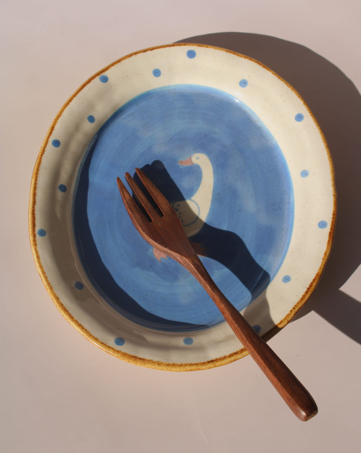 Hand-painted ceramic bowl with blue interior, white duck illustration, and dotted rim, styled in warm natural light.