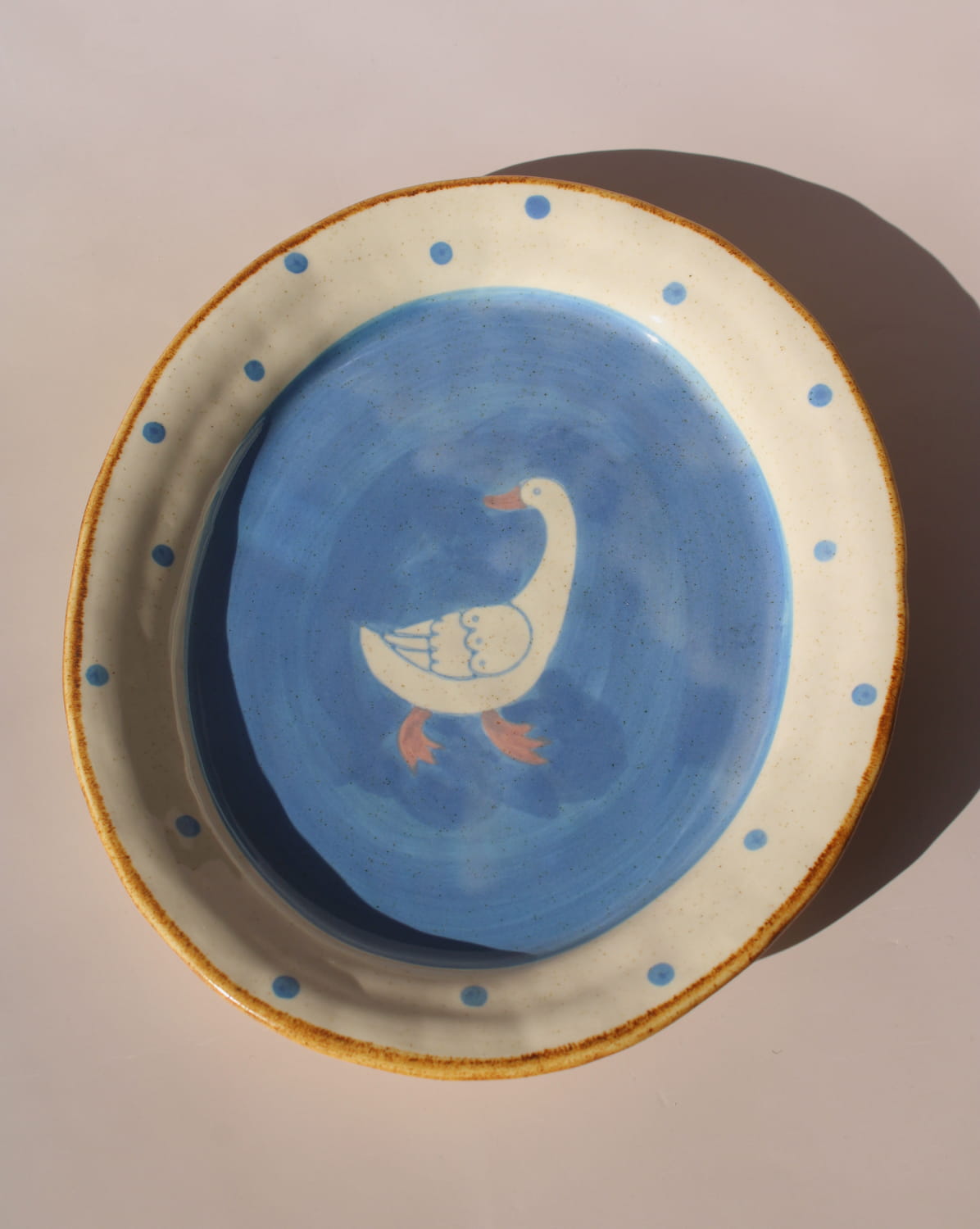 Hand-painted ceramic bowl with blue interior, white duck illustration, and dotted rim, styled in warm natural light.