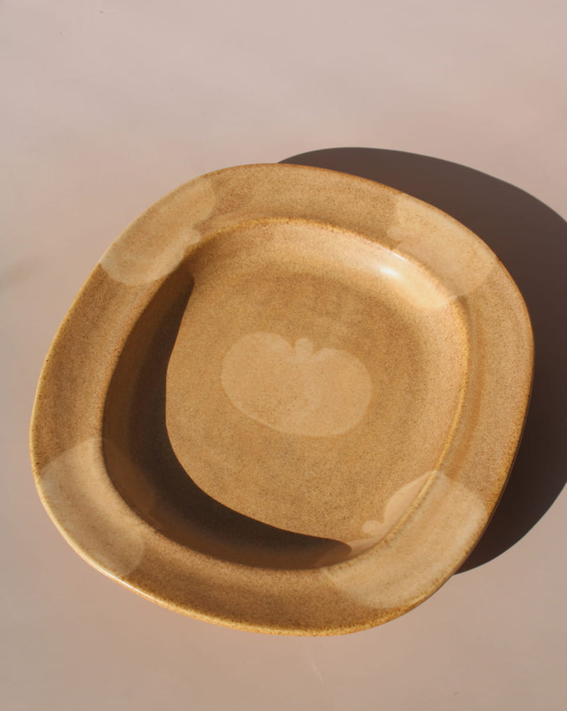 Rustic ceramic plate in warm sand tones featuring a soft apple motif and rounded sculptural shape.
