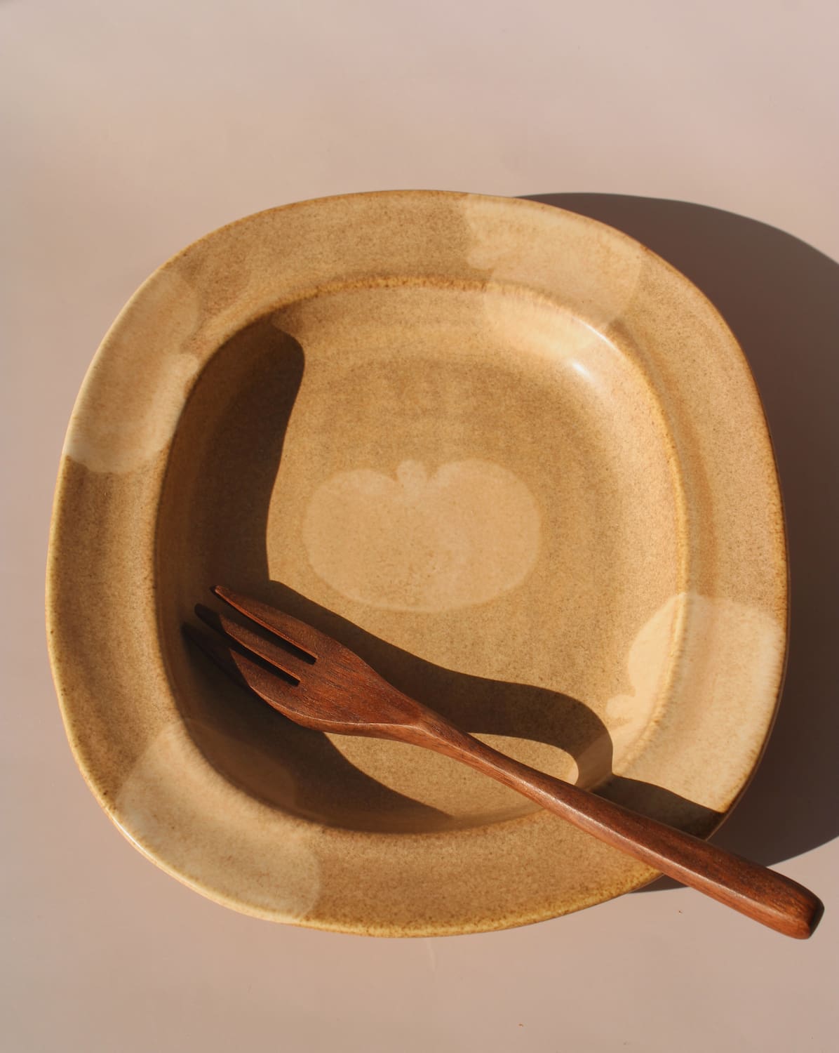 Rustic ceramic plate in warm sand tones featuring a soft apple motif and rounded sculptural shape.