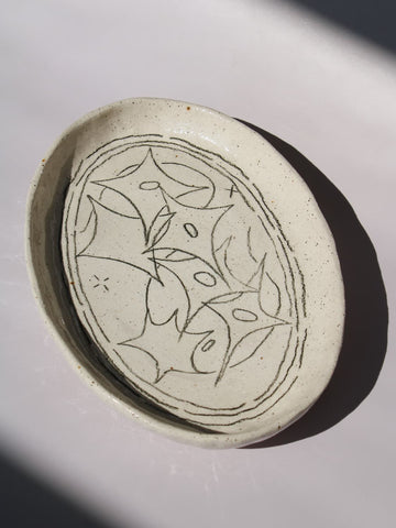 Mythos Ceramic Plate in speckled cream with hand-etched star and leaf motifs, viewed from above on a soft white background.
