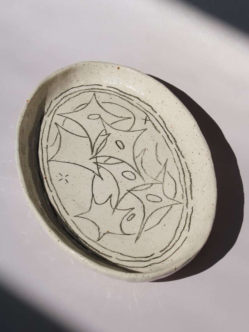 Mythos Ceramic Plate in speckled cream with hand-etched star and leaf motifs, viewed from above on a soft white background.