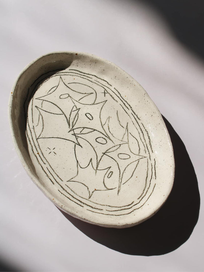 Mythos Ceramic Plate in speckled cream with hand-etched star and leaf motifs, viewed from above on a soft white background.