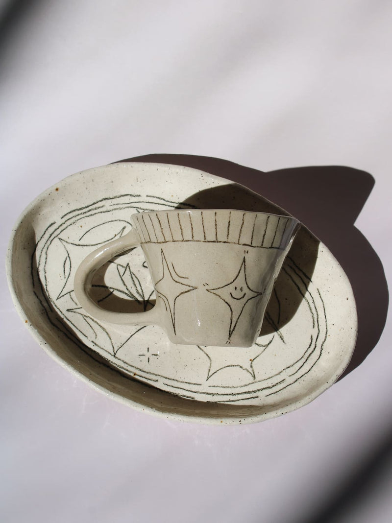 Mythos Ceramic Plate and Astral Ceramic Mug in matching speckled cream with hand-etched star and botanical line drawings, styled together on a soft white background.