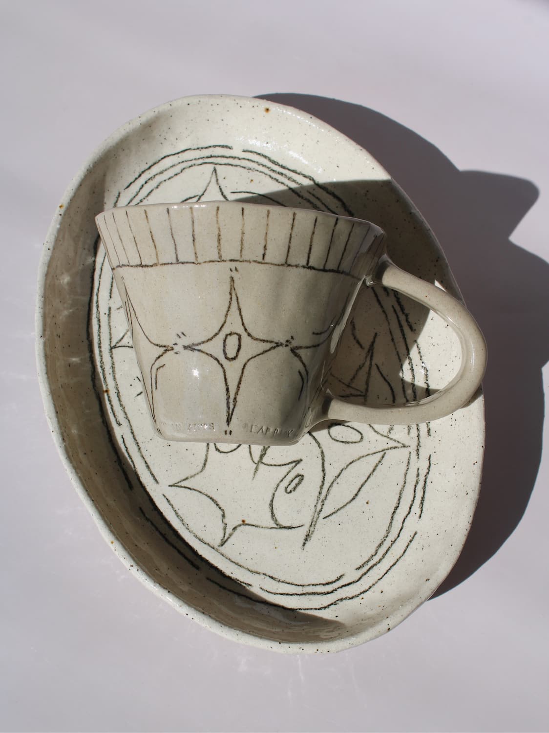 Mythos Ceramic Plate and Astral Ceramic Mug in matching speckled cream with hand-etched star and botanical line drawings, styled together on a soft white background.