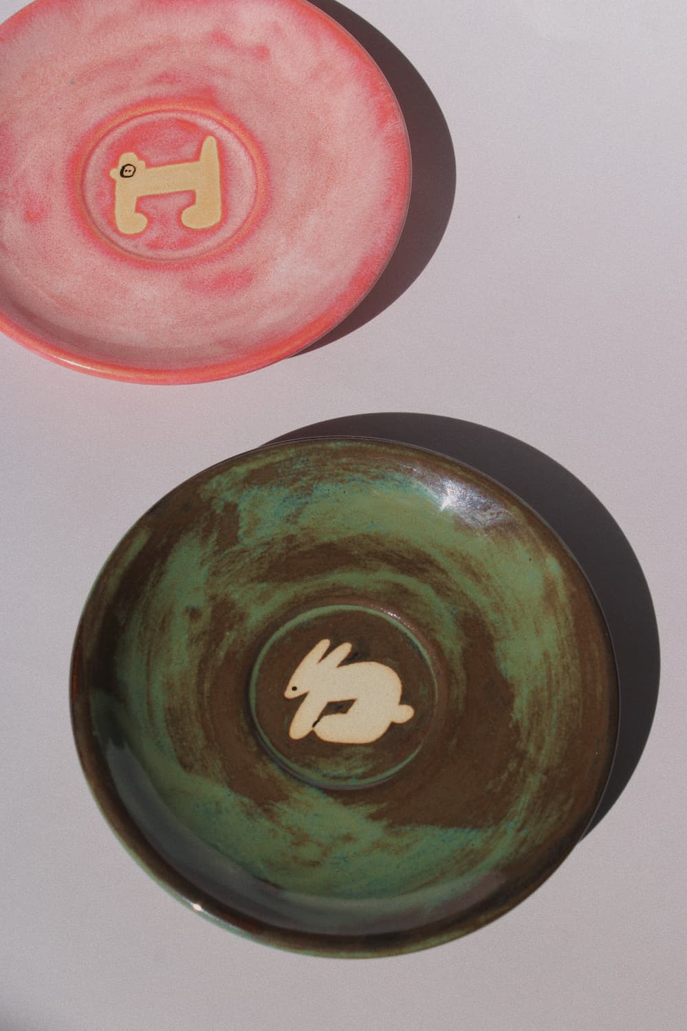 Woodland Rabbit and Candy Monkey Ceramic Plates by Marta Shurpakova – handmade illustrated ceramic plates in earthy green and playful pink tones