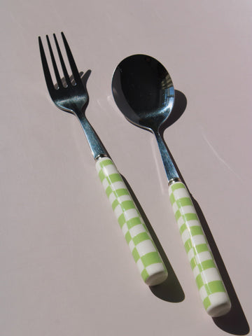 Nico Fork and Spoon Set in stainless steel with green and white checkered handles, on a soft pink background.