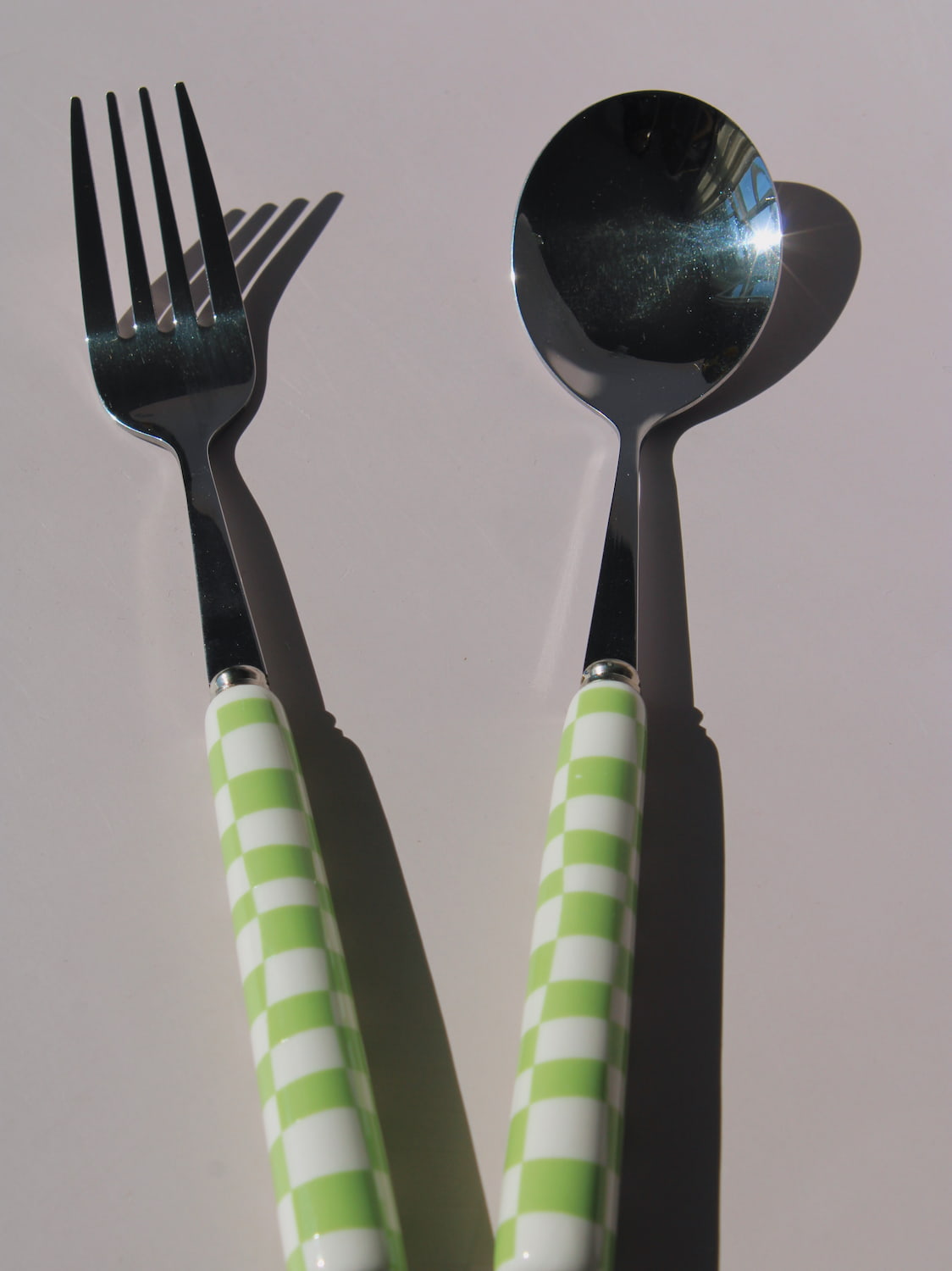 Nico Fork and Spoon Set in stainless steel with green and white checkered handles, on a soft pink background.
