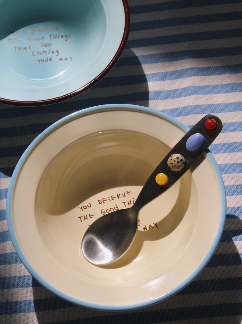 Constella spoon resting in ceramic bowl with soft natural light and striped table setting.