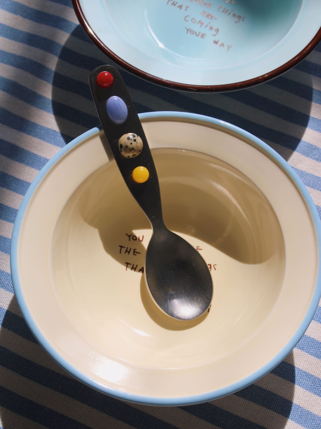 Constella spoon resting in ceramic bowl with soft natural light and striped table setting.