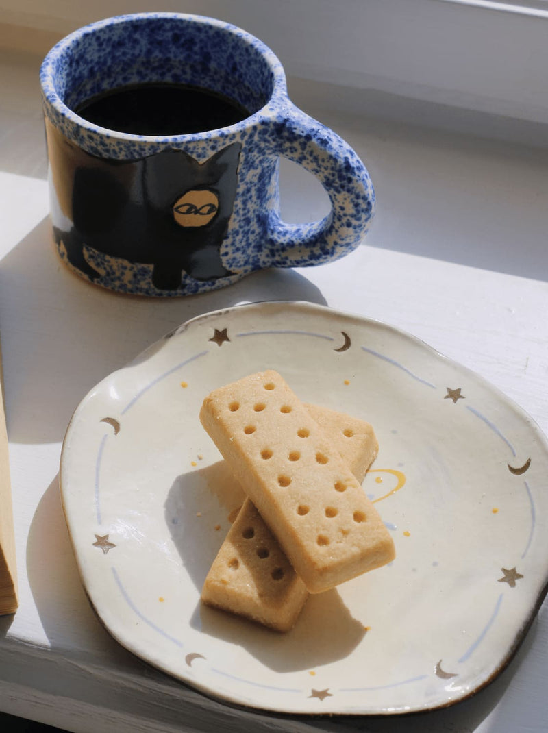 Elio ceramic plate styled with snack and Midnight Cat mug on simple table setting.