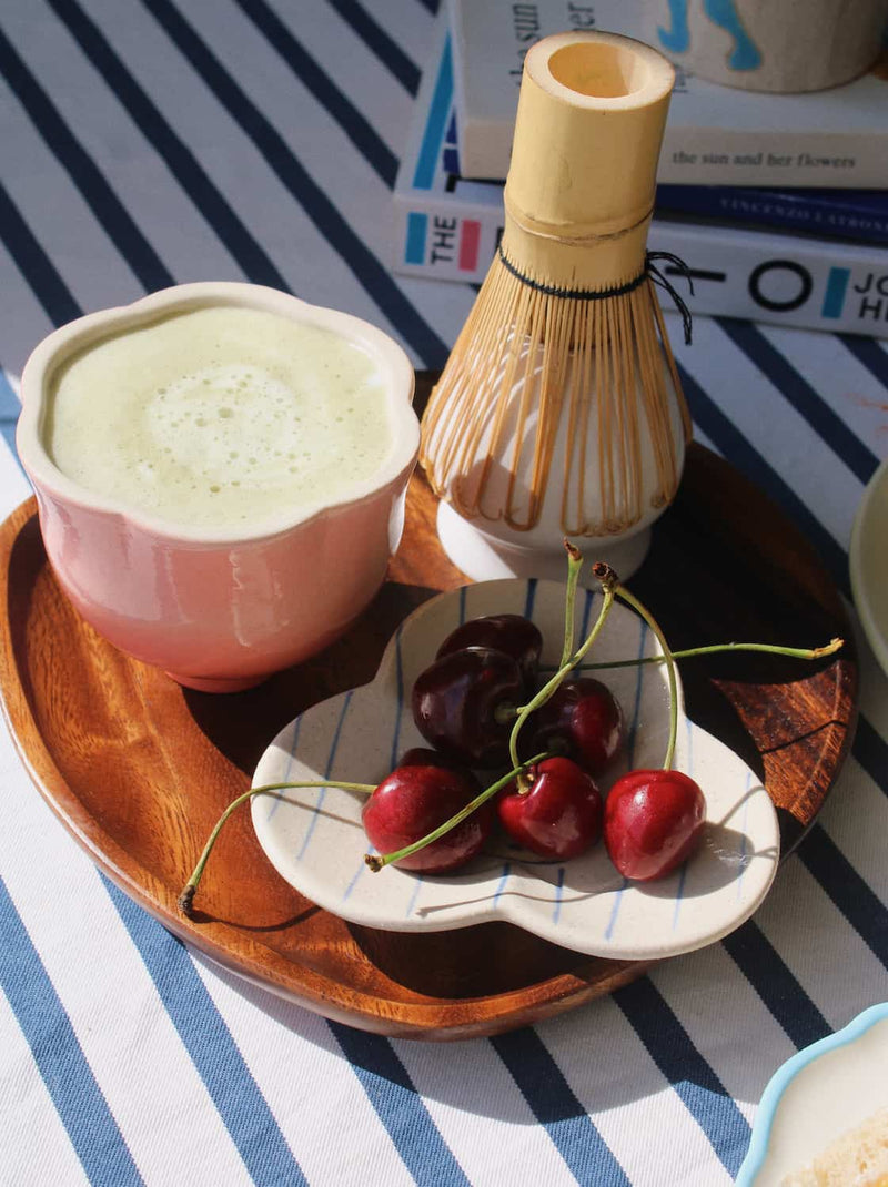 A small ceramic dish with a scalloped edge and thin blue stripes, holding three red cherries and a pale yellow pear on a blue-and-white striped tablecloth.