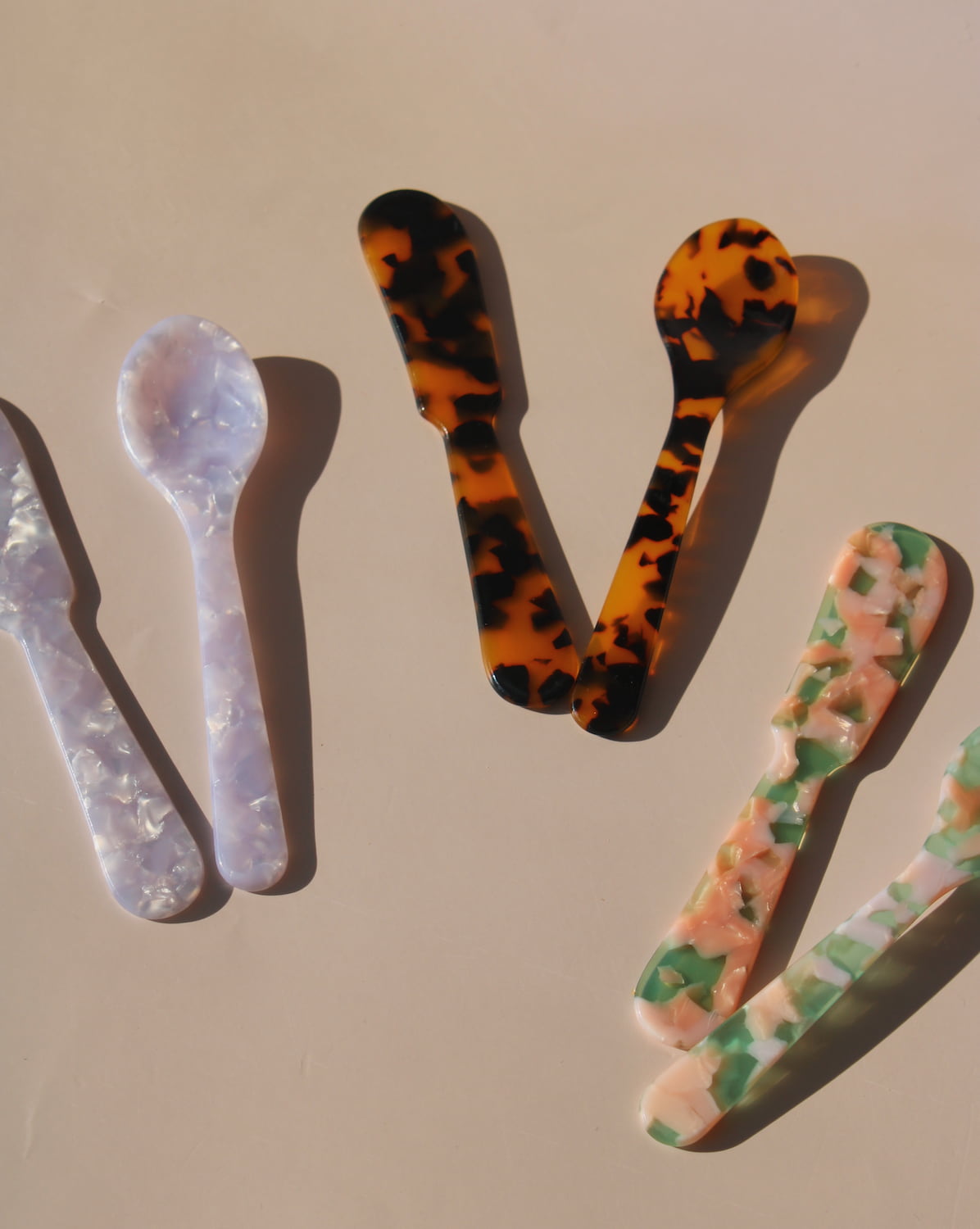 Colorful marbled resin spoons in tortoiseshell, lavender, green, and cream acrylic designs.