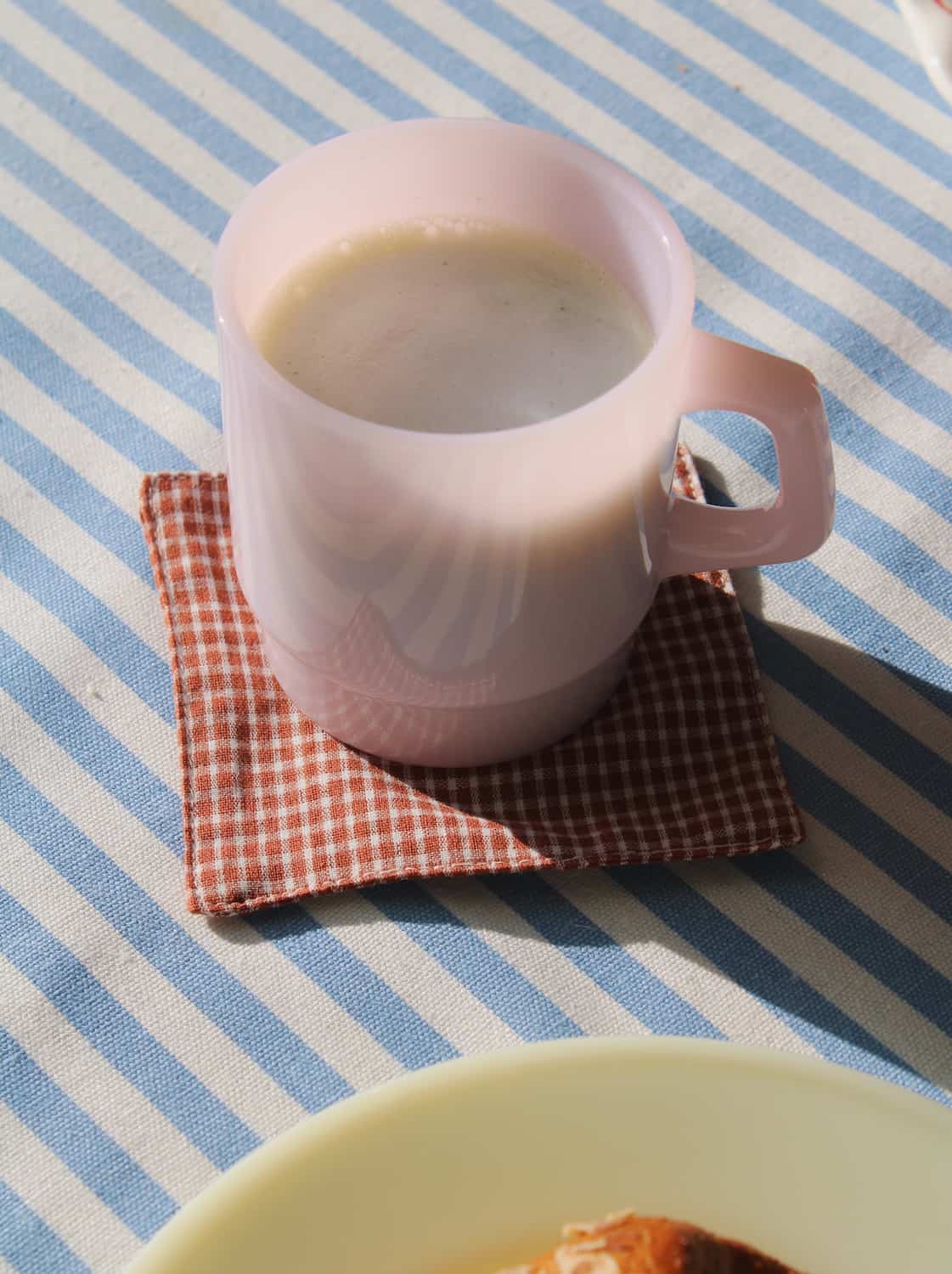 Pink mug with a checkered coaster on a blue and white striped tablecloth