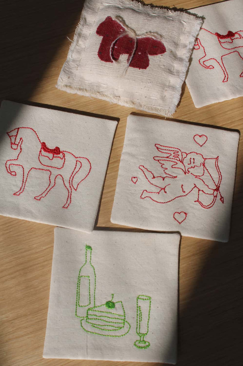 Maison Handsewn Embroidered Coaster with wine motif and Amour Handsewn Embroidered Coaster with cupid embroidery styled together on table.