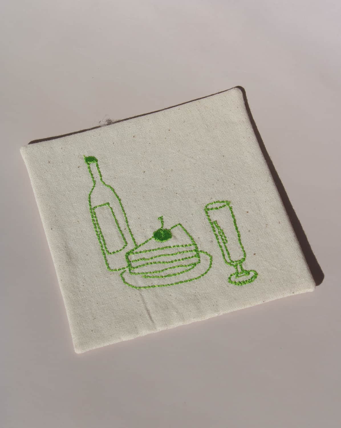 Maison Handsewn Embroidered Coaster with green stitched wine bottle, cake slice, and champagne glass motif on natural cotton fabric.