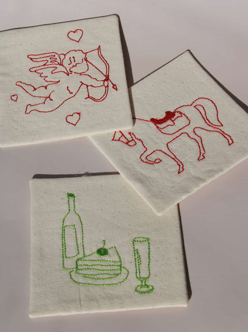 Maison Handsewn Embroidered Coaster with wine motif and Amour Handsewn Embroidered Coaster with cupid embroidery styled together on table.