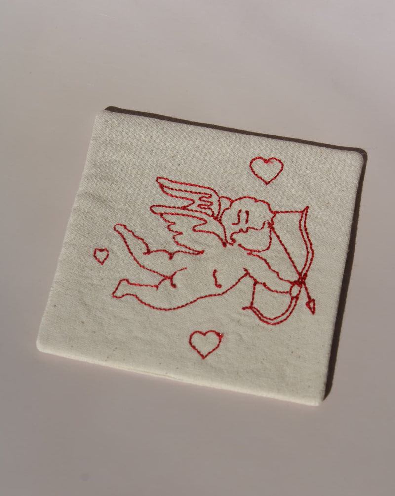 Amour Handsewn Embroidered Coaster with cupid and heart motif stitched in red on natural cotton handmade drink coaster.