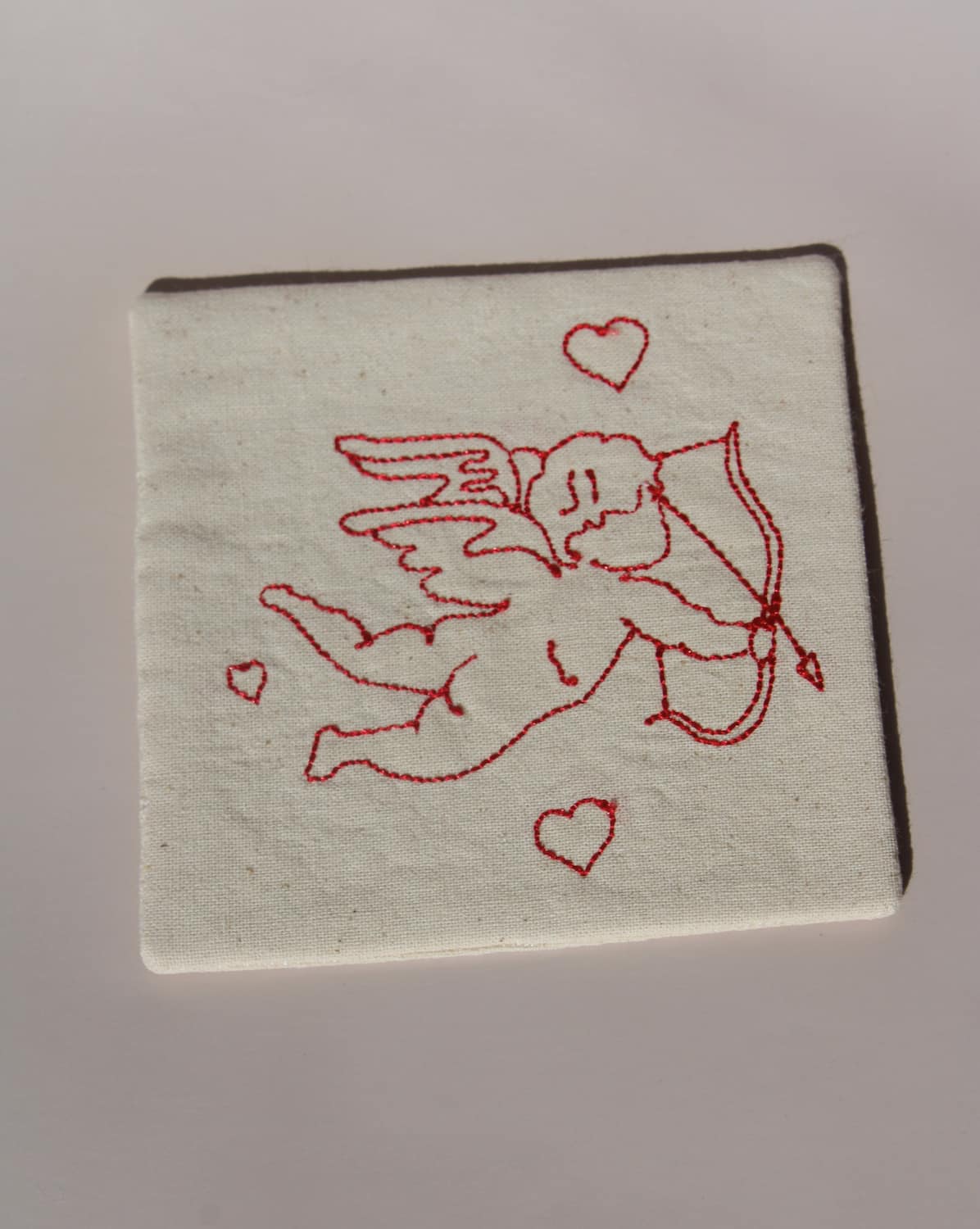 Amour Handsewn Embroidered Coaster with cupid and heart motif stitched in red on natural cotton handmade drink coaster.