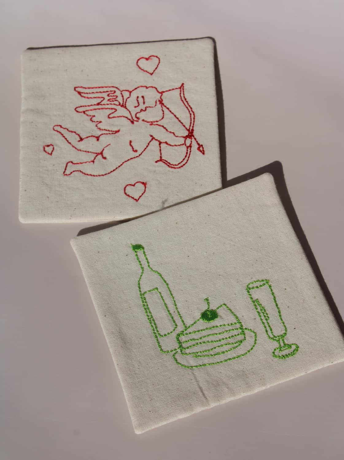 Maison Handsewn Embroidered Coaster with wine and cake embroidery paired with Amour Handsewn Embroidered Coaster featuring cupid motif.
