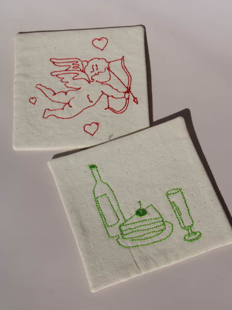 Maison Handsewn Embroidered Coaster with wine and cake embroidery paired with Amour Handsewn Embroidered Coaster featuring cupid motif.