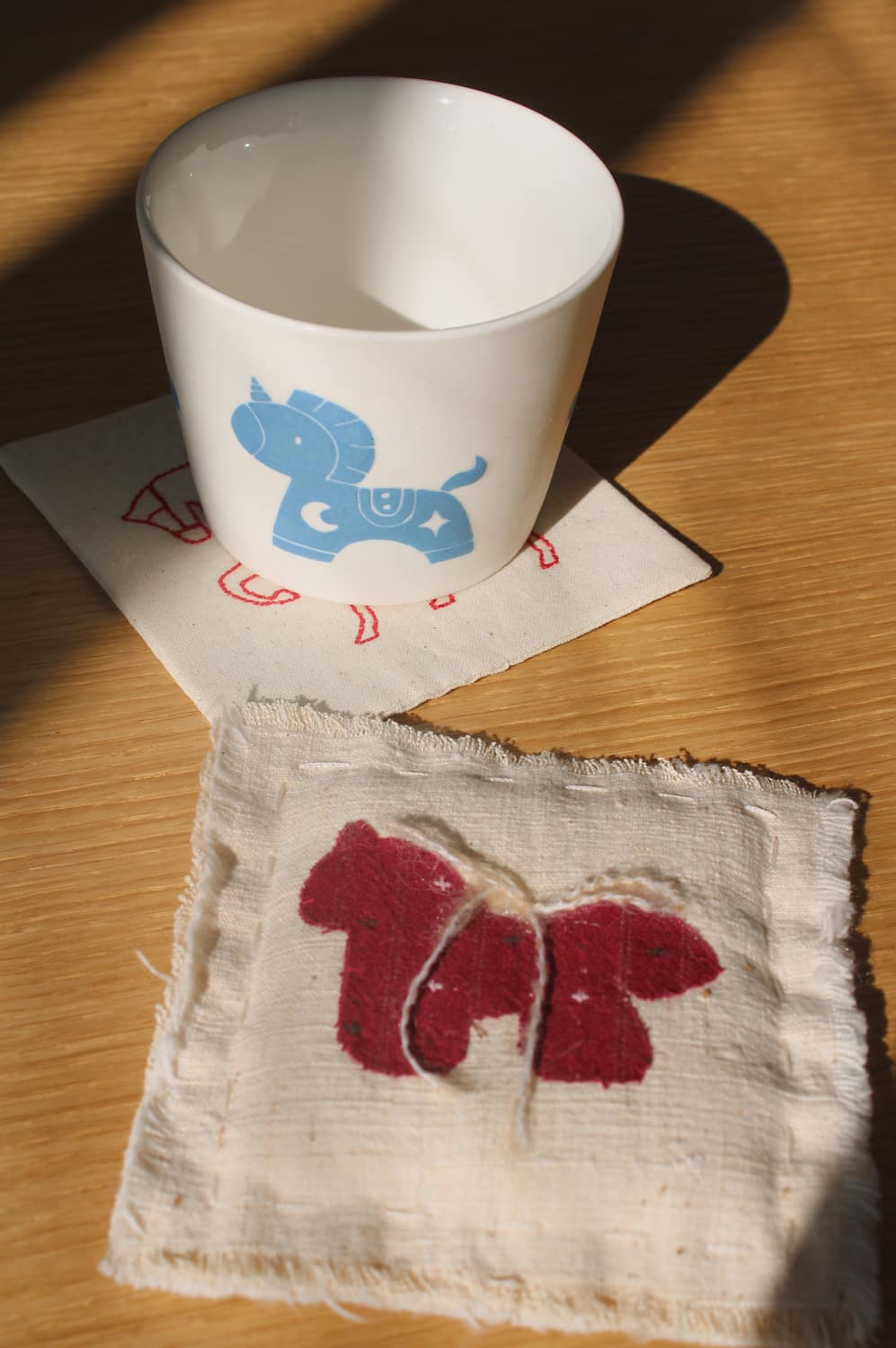 Trotte ceramic cup with blue horse motif placed on Écurie handmade horse coaster, ceramic cup and embroidered textile coaster set.